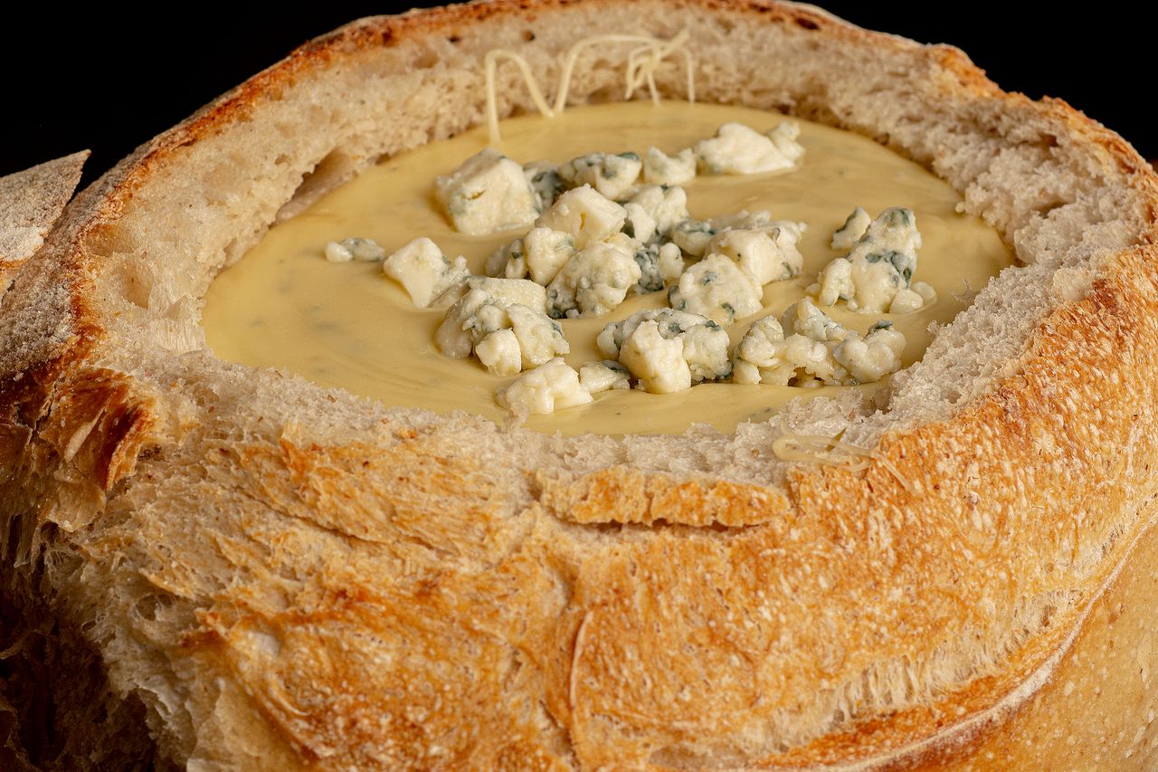Close-up of a bread bowl filled with creamy cheese soup topped with blue cheese.
