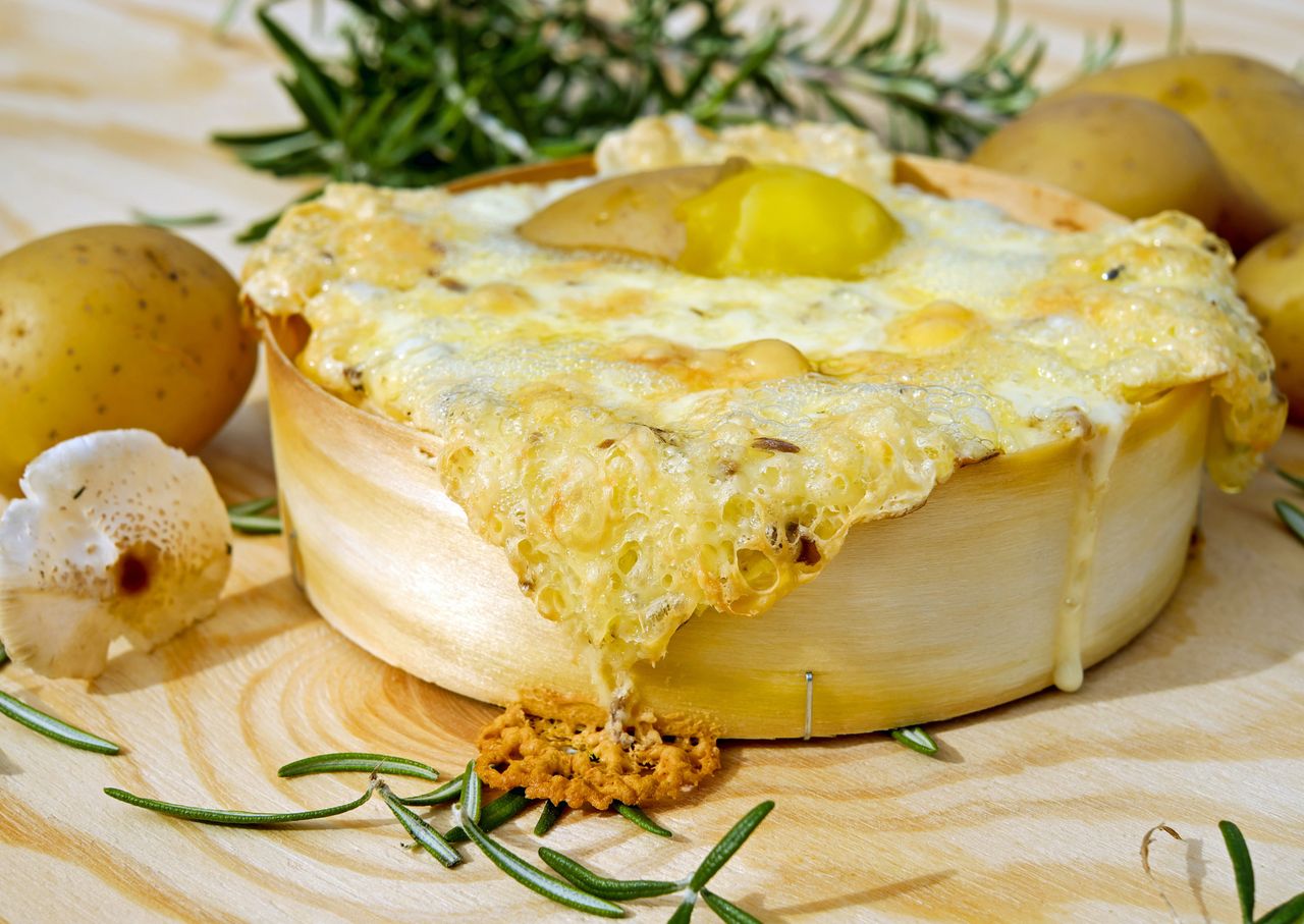 Mouthwatering baked cheese dish with rosemary, potatoes, and mushrooms on a wooden board.